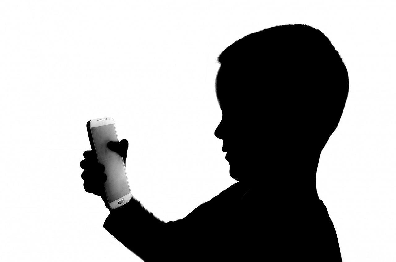 검정색으로 음영처리된 아이의 형상이 손에 휴대폰을 들고 있는 이미지